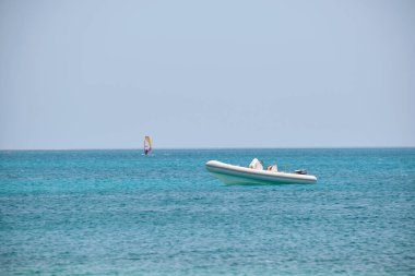 Mavi deniz suyunun dalgalı yüzeyi ve durgun dalgalarda yüzen beyaz sürat teknesiyle deniz manzarası..