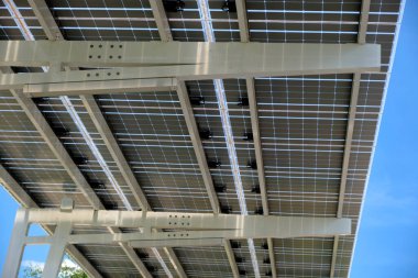 Solar panels installed as shade roof over parking lot for parked electric cars for effective generation of clean electricity. Photovoltaic technology integrated in urban infrastructure.