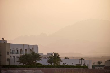 Uzak otel kompleksiyle gün batımı manzarası Mısır çölündeki karanlık dağ zirvelerine karşı.