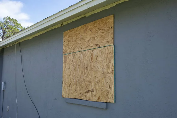 Hurricane shutters made from plywood mounted for protection of house windows. Protective measures before natural disaster in Florida.