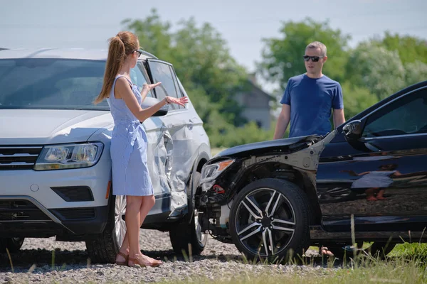 Angry woman and man drivers of heavily damaged vehicles arguing who is guilty in car crash accident on street side. Road safety and insurance concept.