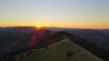 Dağ yamacındaki çoban evleri ve batan güneşle aydınlatılmış çam ormanları. Vahşi dağlarda renkli günbatımının havadan görünüşü. Güzel doğa manzarası.