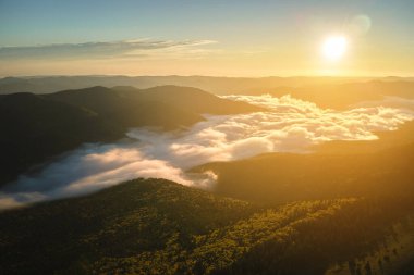 Parlak günbatımında karanlık çam ağaçları üzerinde sisli bir akşamın havadan görüntüsü. Şafakta vahşi dağ ormanlarının inanılmaz manzarası.