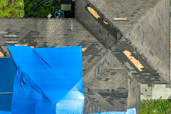 ハリケーンイアンの家の屋根の損傷の空中ビューは アスファルトの帯状疱疹の交換まで雨の水漏れに対する青の保護タープで覆われて — ストック写真