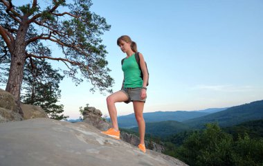 Genç bir kadın dağ yolunda tek başına yürüyüş yapıyor. Dişi yürüyüşçü, vahşi doğa yolundaki akşam manzarasının tadını çıkarıyor. Aktif yaşam konsepti.