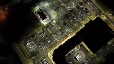 Gece vakti park yeri ve park halindeki birçok arabanın havadan görüntüsü. Araç mekanları ve yönleri için çizgileri ve işaretleri olan süpermerkez alışveriş merkezindeki karanlık otopark..