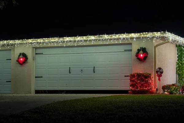 Front yard with brightly illuminated christmas decorations on driveway to house garage. Outside decor of florida family home for winter holidays.