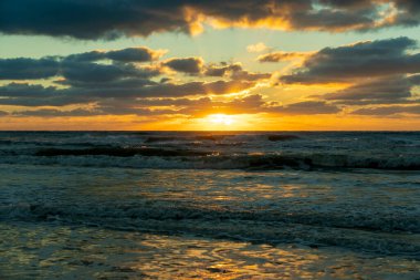 Gün batımında kumlu sahile vuran deniz suyu dalgalarının akşam manzarası.