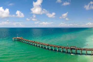 Venice fishing pier in Florida on sunny summer day. Bright seascape with surf waves crashing on sandy beach. clipart