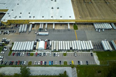 Ülke çapında dağıtım için perakende mal indiren ve yükleyen bir çok dağıtım kamyonuyla büyük ticari yükleme alanının havadan görüntüsü. Küresel ekonomi kavramı.