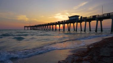 Florida 'daki Venice balıkçı iskelesinde kumlu sahilde güneşli bir gün batımı. Deniz yosunlarıyla kaplı, deniz kıyısına vuran dalgalarla akşam deniz manzarası.