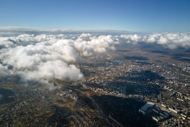 Uzak şehrin yüksek irtifasındaki uçak penceresinden hava manzarası beyaz kabarık kümülüs bulutlarıyla kaplı..