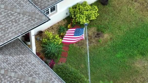 フロリダのプライベートハウスの前庭で振るアメリカの国旗 アメリカのスターやストライプの空中ビュー 民主主義のシンボルとしてのバナー — ストック動画