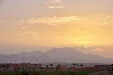 Uzak otel kompleksiyle gün batımı manzarası Mısır çölündeki karanlık dağ zirvelerine karşı.