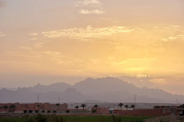 Sunset landscape with remote hotel complex against dark mountain peaks in egyptian desert.