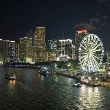 Aerial view of Skyviews Miami Observation Wheel at Bayside Marketplace with reflections in Biscayne Bay water and high illuminated skyscrapers of Brickell, citys financial center at night.