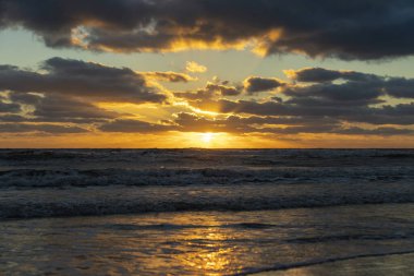 Yumuşak akşam deniz dalgalarının kumlu sahilde ezdiği okyanus batımı manzarası..