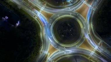 Gece ağır trafiği hızla hareket ettiren kavşağın hava görüntüsü. Aydınlatılmış kentsel dairesel ulaşım kavşağının zamanlaması.