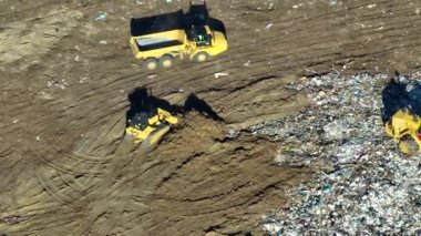 Katı atık imha tesisi. Çöplük yönetimi için çöplük alanı. Buldozer traktörleri yerin altına büyük miktarda çöp gömüyor. Modern tüketiciliğin çevre üzerindeki zararlı etkisi.