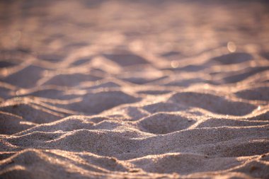 Sahil kenarını kaplayan temiz sarı kum yüzeyi akşam ışığıyla aydınlatılıyor. Seyahat ve tatil kavramı.