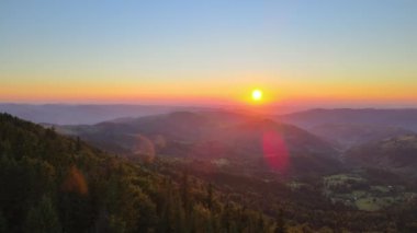 Parlak batan güneşle aydınlanan karanlık çam ormanı. Vahşi dağlarda renkli günbatımının havadan görünüşü. Güzel doğa manzarası.