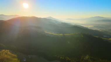 View from above of Ukrainian Carpathian mountains with wooded hills and traditional village homes at autumnal sunset. Brightly illuminated pine woods with scattered local settlement houses.