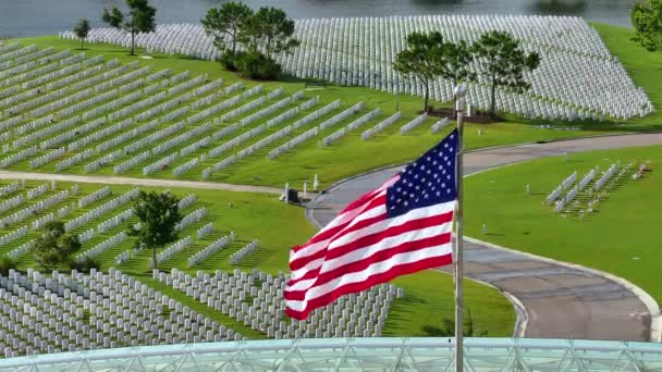 陸軍の国立墓地の上に広がる大きなアメリカの旗は 緑の草の上に白い墓石が並んでいます メモリアルデーのコンセプト — ストック動画