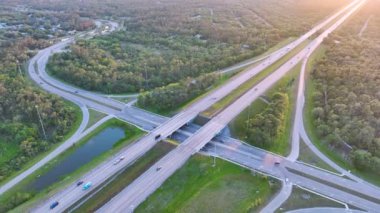 Aerial view of freeway overpass junction with fast moving traffic cars and trucks in American rural area at sunset. Interstate transportation infrastructure in USA.