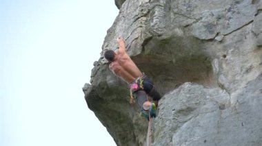 Genç adam dik kayalık dağ duvarına tırmanıyor. Erkek tırmanışçı zorlu rotayı aşar. Ekstrem spor konseptine dalmak.