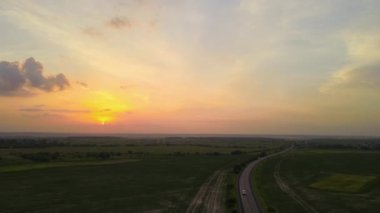 Gün batımında tarlalar arasında hızlı giden arabalarla şehirlerarası yol manzarası. Akşamları otoban trafiğinin insansız hava aracı görüntüsü.