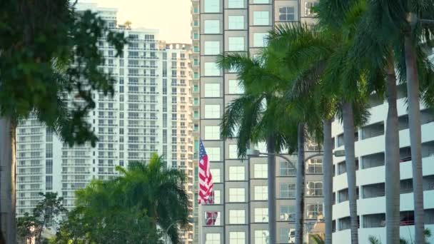 マイアミのスカイラインの前で振るアメリカの国旗 アメリカのスターやストライプの空中ビュー 民主主義のシンボルとしてのバナー — ストック動画