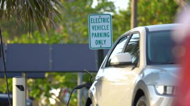 Electric plug-in car charging with electricity from solar renewable power source parked on city street.