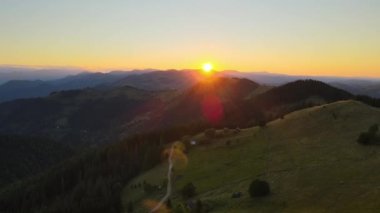 Yamaçtaki eski köylü evinin havadan görünüşü. İnanılmaz bir dağ manzarası. Vahşi Ulusal Park Dağları 'nda parlak renkli gün batımı. Sarı batan güneşle aydınlatılmış koyu ladin ormanları..