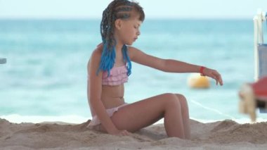 Happy child girl in bikini swimsuit playing with sand on seaside beach during summer tropical vacation.
