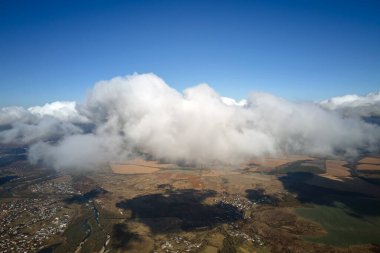 Yükseklerdeki uçak penceresinden, yağmurdan önce oluşan kabarık kümülüs bulutlarıyla kaplı uzak şehrin hava manzarası..