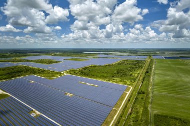 Aerial view of sustainable electric power plant between agricultural farm fields with solar photovoltaic panels for producing clean electrical energy. Renewable electricity with zero emission concept.