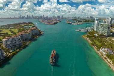 Güney Sahili yakınlarındaki Miami limanı ana kanalından büyük konteynır gemisinin hava görüntüsü. Şehir merkezindeki liman ve gökdelenlerde lüks oteller ve apartmanlar..
