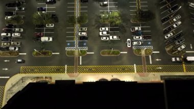 Parlak bir şekilde aydınlatılmış park yerindeki alışveriş merkezinin önünde gece park edilmiş birçok arabanın en iyi görüntüsü. Tüketim ve piyasa ekonomisi kavramı.