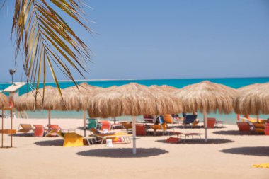 Yazın mavi renkli gökyüzüne karşı dinlenen güneşli deniz kıyılarında saman gölgesi şemsiyeleri..