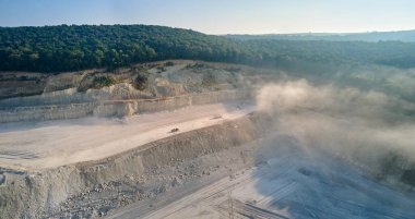 Kazı araçları ve çöp kamyonlarıyla inşaat endüstrisi için kireçtaşı malzemelerinin açık maden sahası görüntüsü.