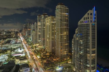 Yoğun trafik ve yüksek gökdelen binaları ile aydınlık şehir caddesinin yukarıdan görüntüsü Florida, ABD 'de Sunny Isles Beach şehir merkezinde. Gece vakti Amerikan turist bölgesi.