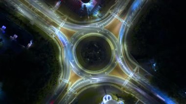 Şehir caddesinin kavşağındaki trafiğin en üst görüntüsü gece hızlı hareket eden arabalarla. Aydınlatılmış kentsel dairesel ulaşım kavşağının zamanlaması.