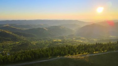 Offroad yolu tepenin üstünden geçiyor. Parlak batan güneşle aydınlanan karanlık toprak yol. Vahşi dağ ormanlarında gün batımı manzarası inanılmazdır. Güzel doğa manzarası.