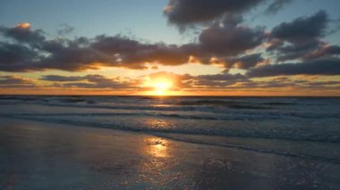 Gün batımında kumlu sahile vuran deniz suyu dalgalarının akşam manzarası.