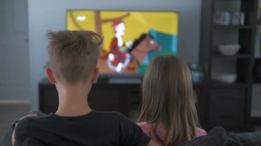 Evde televizyon izleyen erkek ve kız kardeşlerin dikiz görüntüsü. Çocuklar kanepede oturup çizgi film izliyorlar..