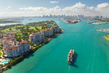 Güney Sahili yakınlarındaki ana kanaldan Miami limanına giren ticari konteynır gemisi. Lüks oteller, rıhtımdaki konut binaları ve şehir merkezindeki yüksek gökdelen kuleleri..