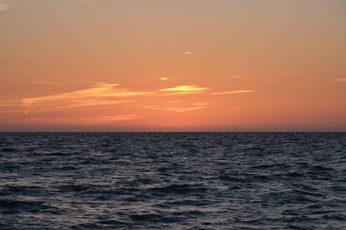 Dramatic bright red sky at ocean sunset, soft evening clouds over sea dark water.