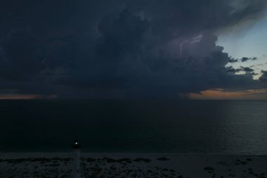 Deniz kıyısındaki uzun deniz feneri fırtınalı bir gecede ticari gemilerin seyrüsefer için yanıp sönen ışık. Okyanus üzerinde şimşekler çakan fırtına gemiler için tehlike arz ediyor..