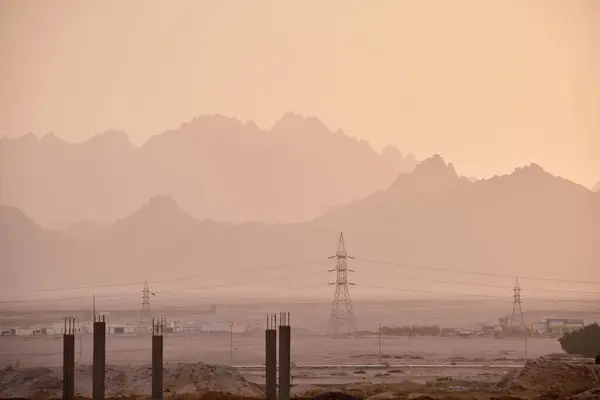 Sunset landscape with dark mountain peaks in egyptian desert and high voltage power lines.