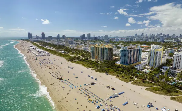 Tourism infrastructure in southern USA. South Beach sandy surface with tourists relaxing on hot Florida sun. Miami Beach city with high luxury hotels and condos.